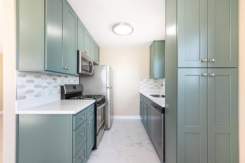 A kitchen with green cabinets and a white counter.