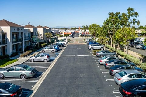 A parking lot with cars parked in rows and apartment buildings in the background. at Whispering Fountains Lakewood, Lakewood Bar, CA 90805
