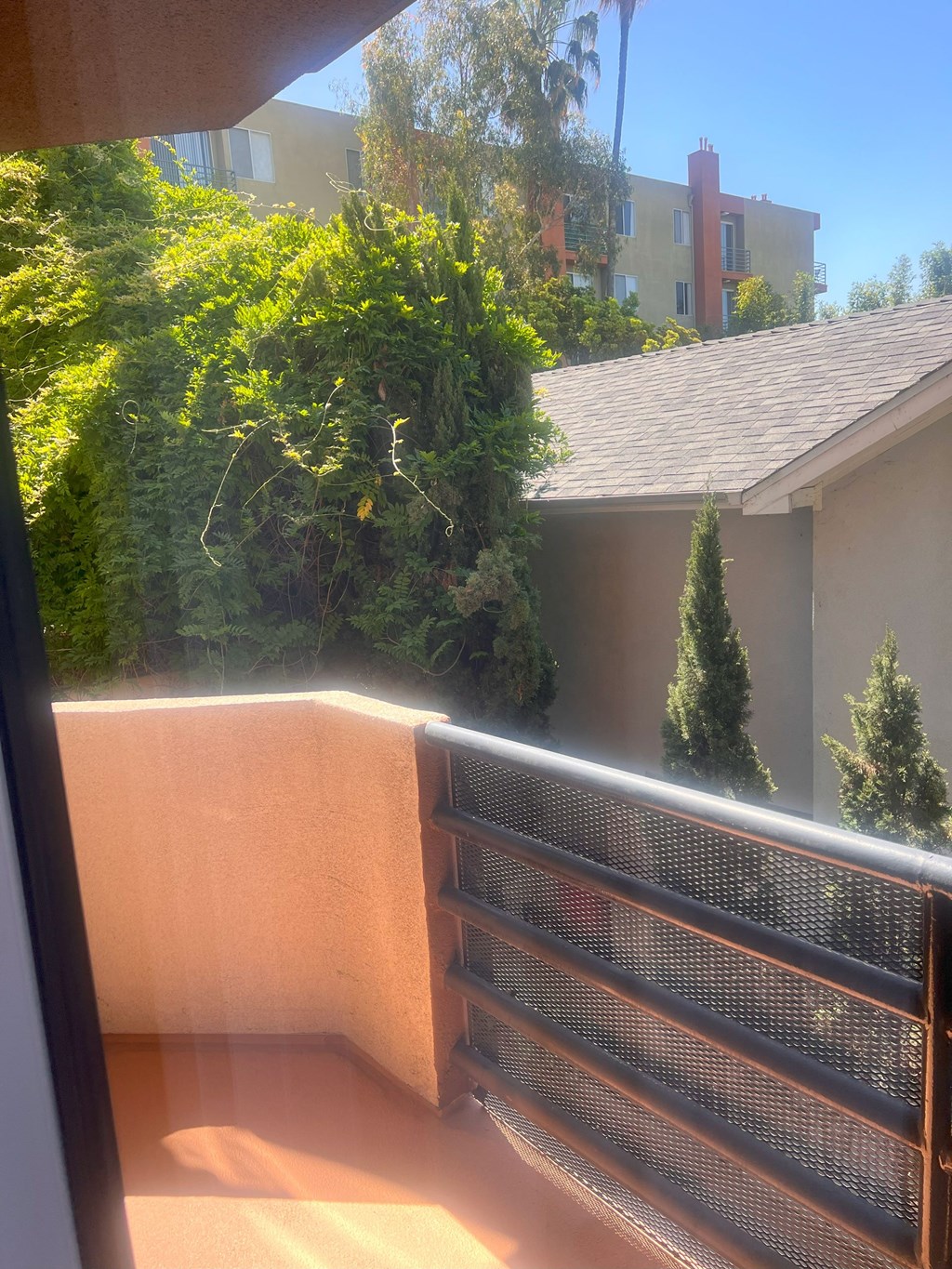 A balcony with a metal railing and a view of a building and trees.