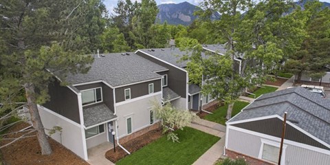 A modern house with a grey roof and white walls is surrounded by trees.