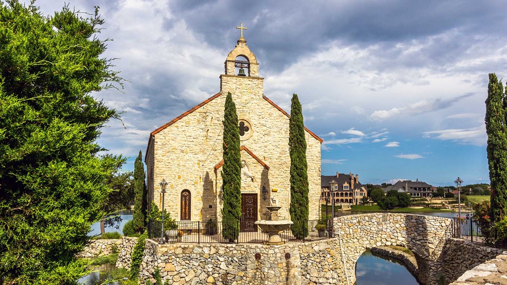 Looking straight on at the front of the chapel. It has a stone foundation and is surrounded by water, a small bridge on the right connecting it.