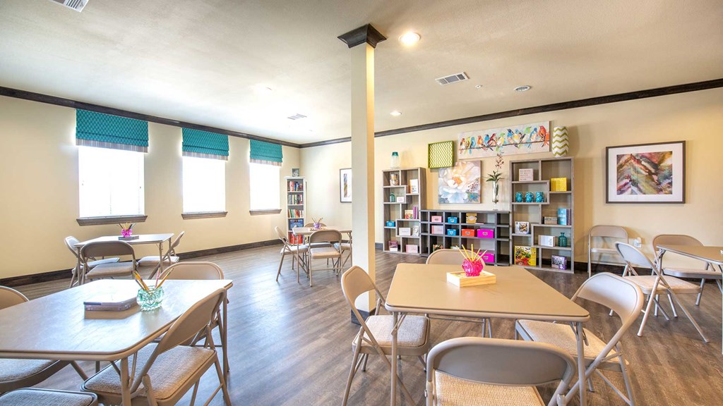 A number of folding chairs and tables around an open room. There is a large shelf in the back with various craft supplies.