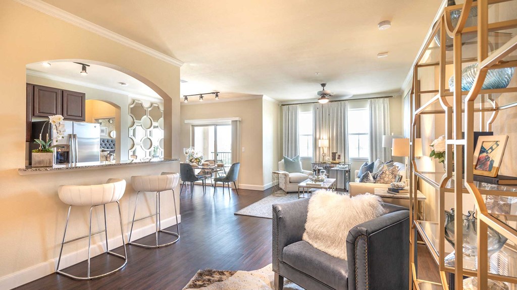 A living room in a residence at Bell Tower Reserve. The kitchen counter with bar stools is the the left, a bookshelf with club chair on the right. Additional sitting areas are seen in the background.