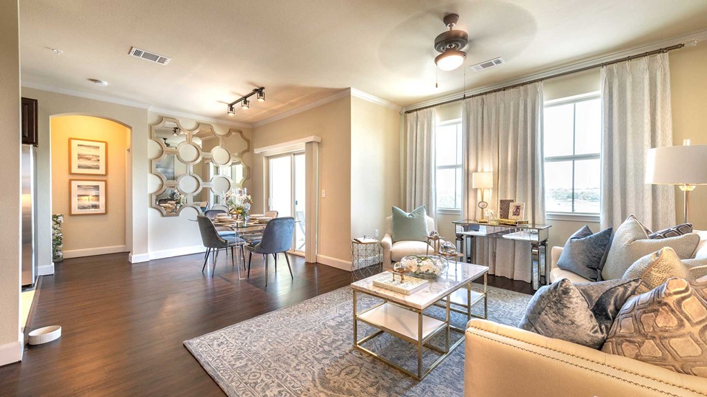 A living room in a residence at Bell Tower Reserve. A couch and sitting area is on the right with a dining set off to the left in front of a sliding glass door.
