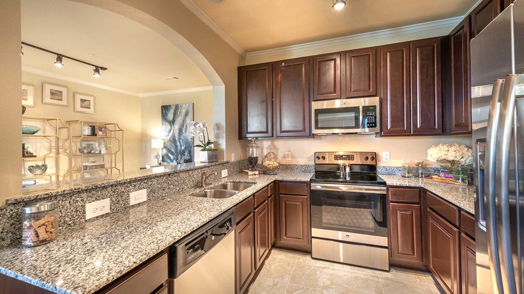 Looking into the kitchen of a residence at Bell Tower Reserve. The kitchen bar is to the left with an opening to the living room. The refrigerator is on the right, the oven and microwave ahead and the dishwasher under the counter on the left.