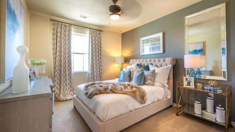 A bedroom in a residence at Bell Tower Reserve. A dresser is on the left, a window ahead and the bed is on the right. A ceiling fans spins above.