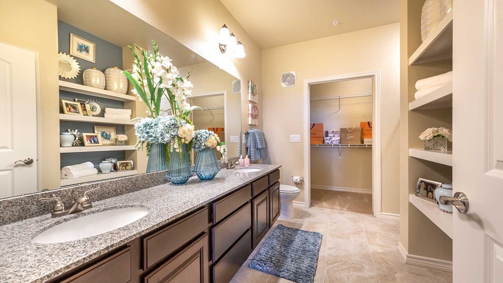 Looking through a bathroom in a residence at Bell Tower Reserve. The double sink vanity lines the left side with a linen closet ahead at the end. Built-in shelves line the right wall.