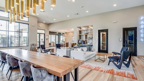 Contemporary apartment clubhouse with oversized communal table, lounge seating, coffee station, and modern pendant lighting in an open-concept space.