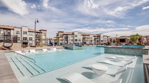 Outdoor pool and lounge area at The Wright in Centennial, Colorado featuring in-water seating, modern landscaping, and contemporary apartment residences in the background.