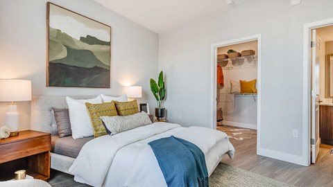 Modern bedroom interior at The Wright featuring contemporary furnishings, wood-style flooring, a walk-in closet, and soft natural lighting.