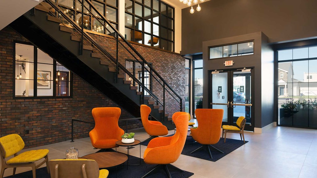 The lobby at Moda at the Hill with two lounge seating areas in front with orange and yellow chairs. The front door is off to the right and a stairway leads up in the background.
