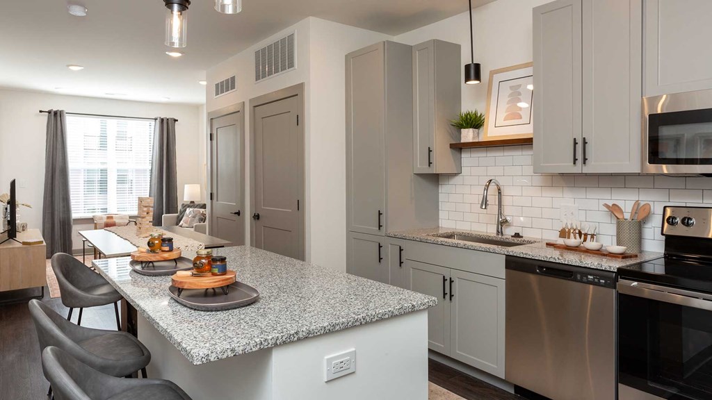 Looking through the kitchen into the living room across the kitchen island. The kitchen is on the right. There are two place settings on the island. A couch and chair are seen in the back near the window.