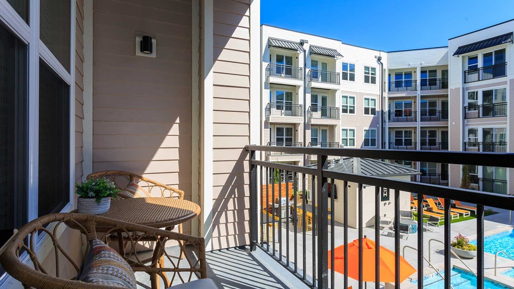 Looking from a balcony in a residence down to the pool in the courtyard. There is wicker furniture on the balcony. The sky is clear blue.