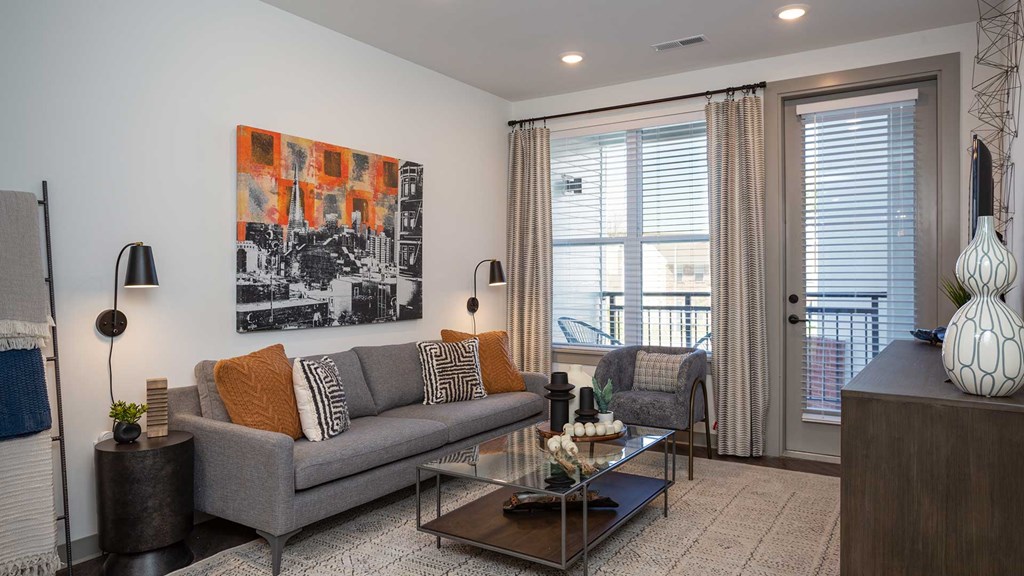 The living room with a couch beneath a large piece of art on the left and the windows and doors to the balcony on the right.