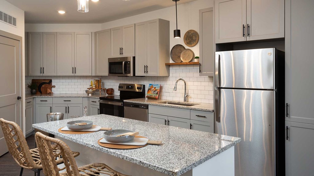 Looking across the kitchen island into the kitchen. The cabinets are modern grey and the appliances are stainless steel.