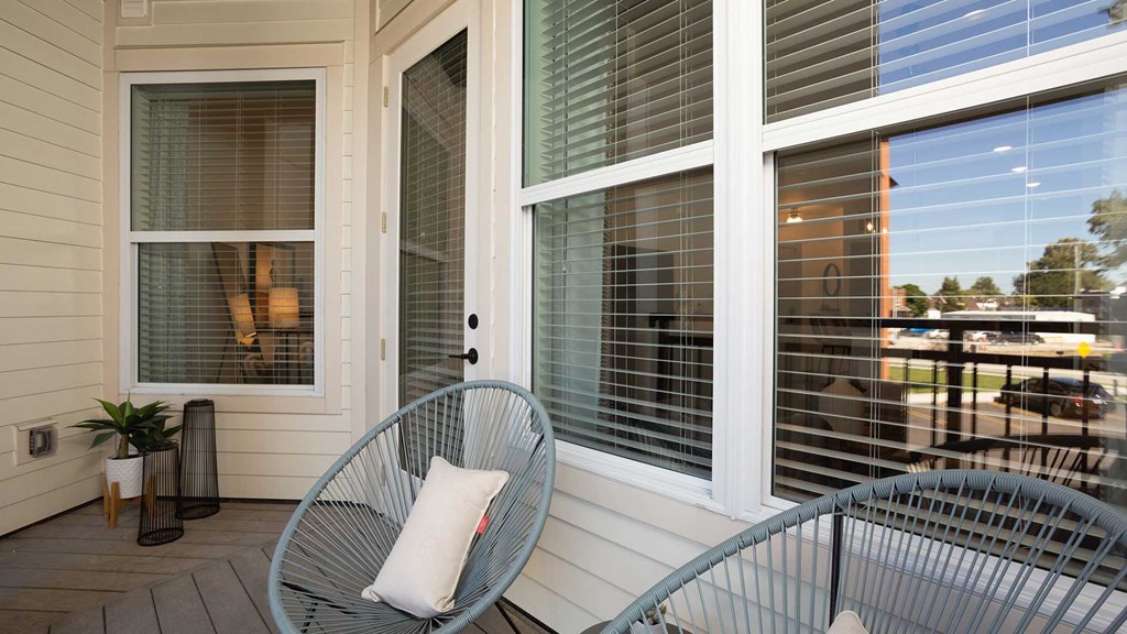 Looking back into the windows while standing on the balcony outside the residence. There are two outdoor chairs in front.