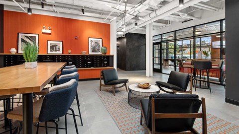 Looking out towards the main Lobby from the Clubroom at Wrigleyville Lofts. A high-top table is on the left with several club chairs in the front. The far wall is orange and also holds mailboxes for residents.