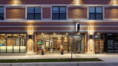 Looking at the front entrance to Wrigleyville Lofts at night from across the street. The lobby and lounge can be seen through the windows.