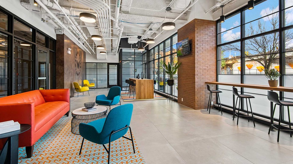 Looking down the main lobby at Wrigleyville Lofts. There are various pieces of brightly colored lounge furniture along the left. The windows to the outside are along the right with a stools along a bar.