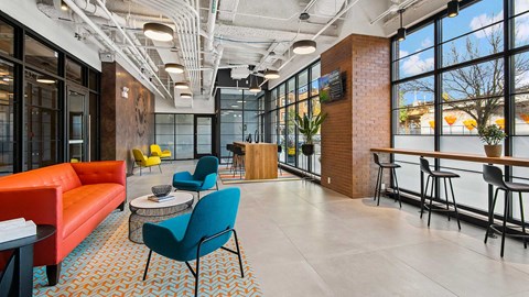 Looking down the main lobby at Wrigleyville Lofts. There are various pieces of brightly colored lounge furniture along the left. The windows to the outside are along the right with a stools along a bar.