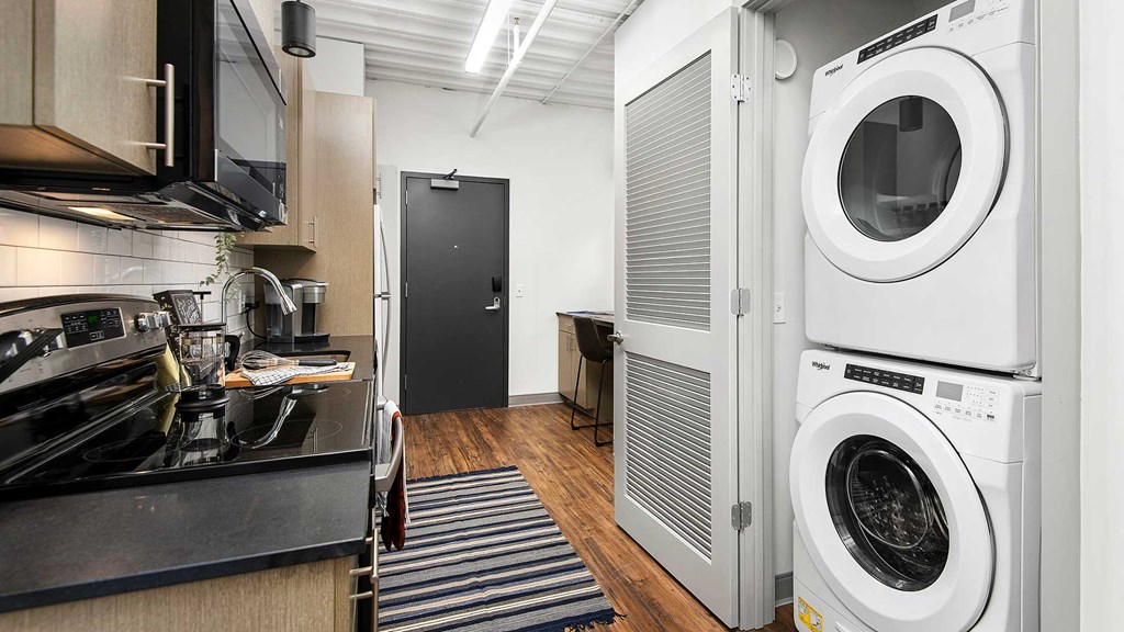 Looking through the kitchen in a residence at Wrigleyville Lofts. The kitchen counter and appliances are along the left and a stacked washer and dryer are seen in an open closet on the right.
