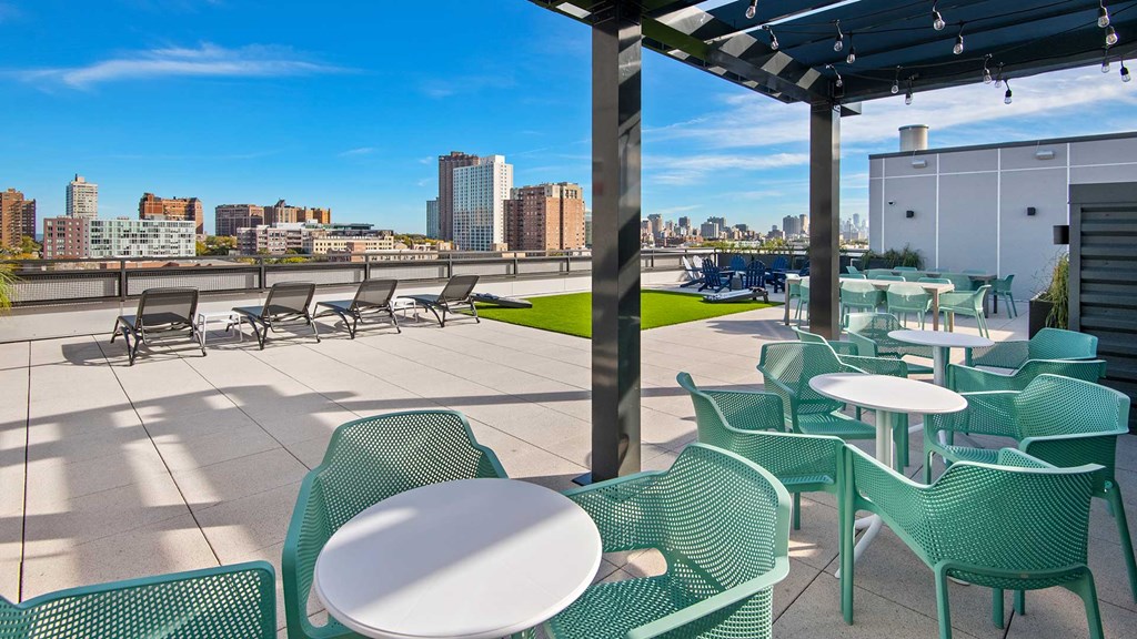 Looking out from under the pergola on the rooftop deck at Wrigleyville Lofts. A few cafe tables sit in the foreground with the rest of the deck beyond. Chicago buildings can be seen in the distance.