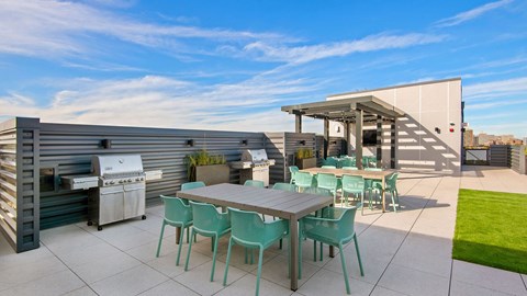 The outdoor kitchen and grilling areas on the rooftop deck at Wrigleyville Lofts. Two outdoor dining tables sit ahead of grills. A television viewing area is behind.