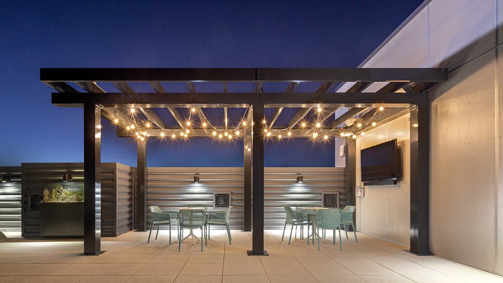 Looking at the pergola on the rooftop deck at Wrigleyville Lofts at night. A few cafe tables sit underneath. below lights.