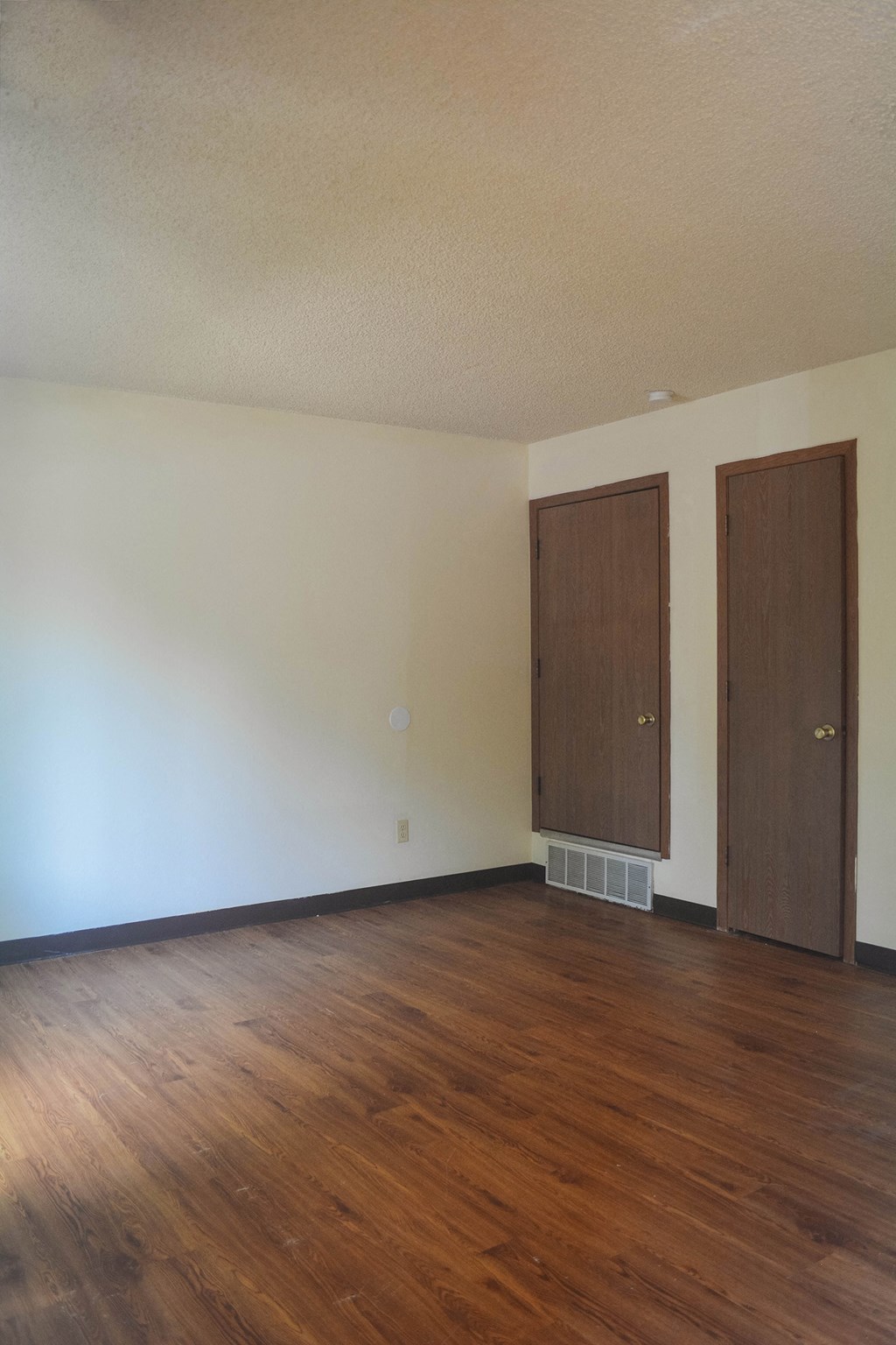 an empty living room with wood flooring and two doors