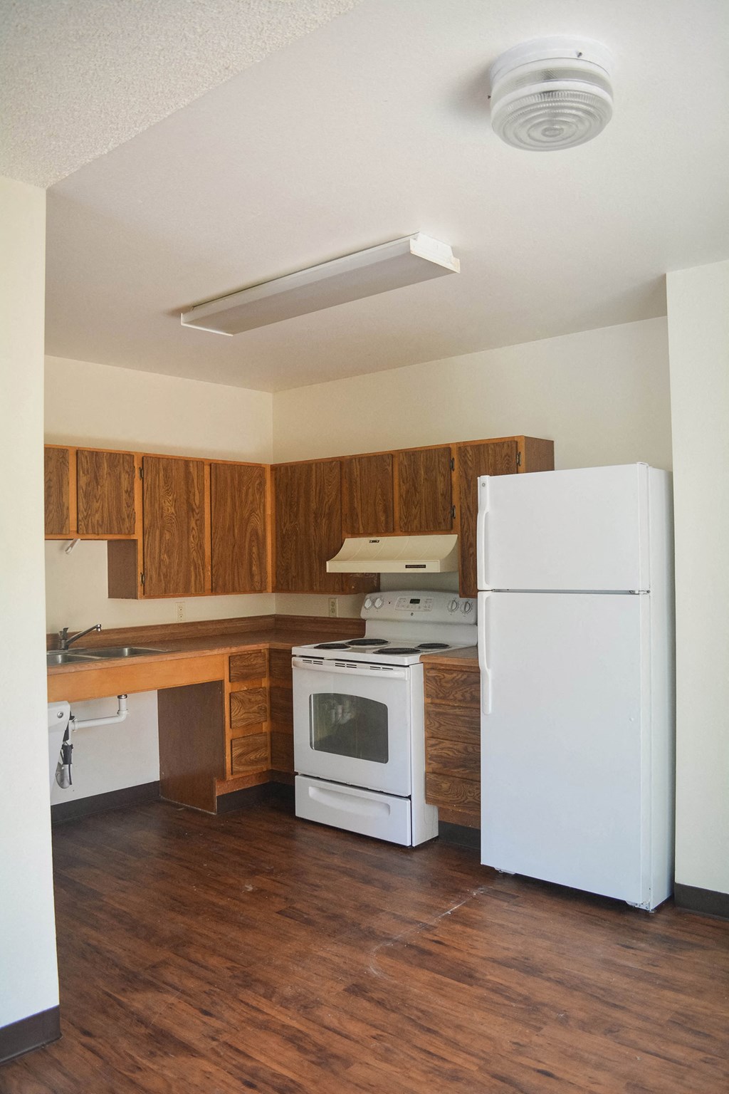 an empty kitchen with white appliances and wooden cabinets