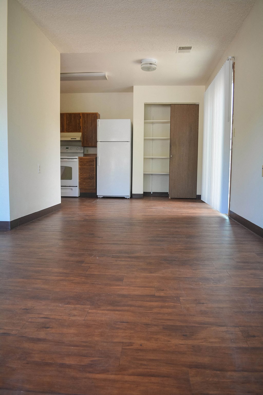 an empty living room with wooden floors and a white refrigerator