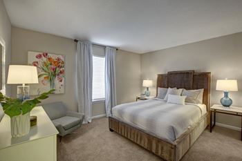 A bedroom with a large bed, a nightstand, and a chair.