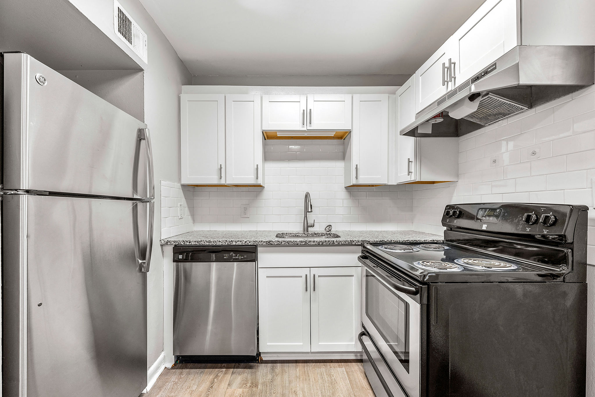 A kitchen with a black stove top oven and a stainless steel refrigerator.