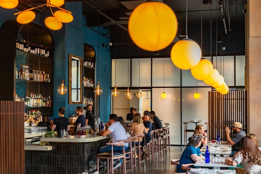A group of people are sitting at a bar with a blue wall behind them.