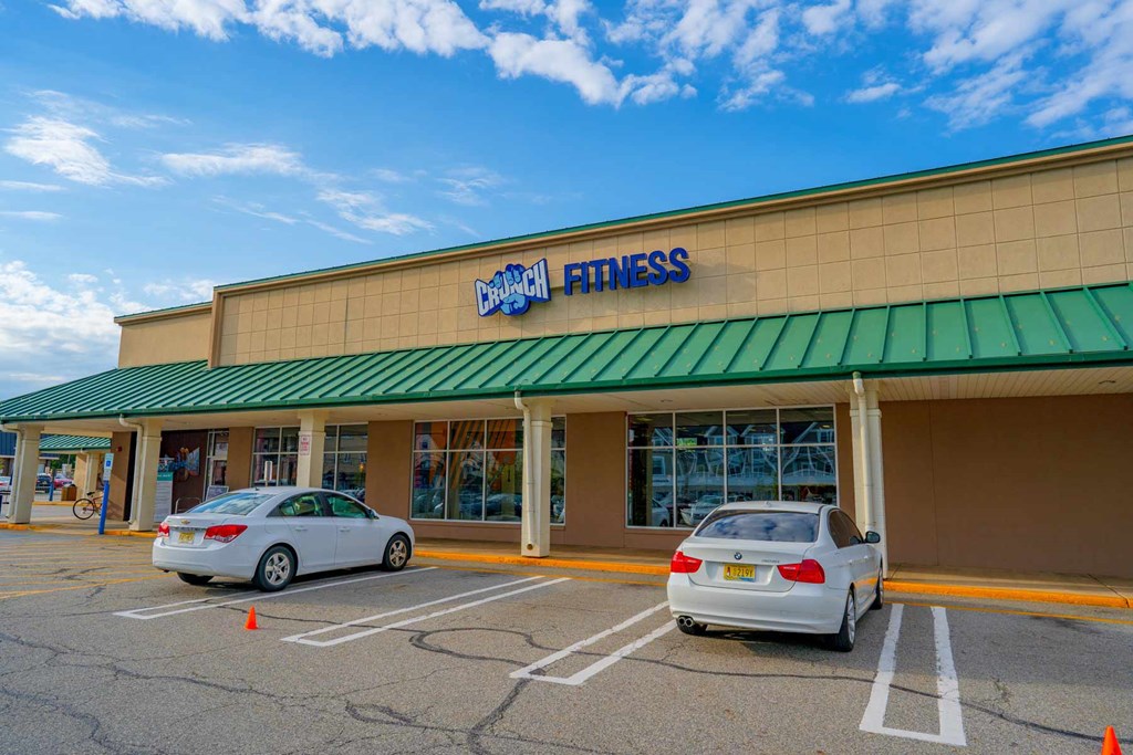 A car is parked in front of a building with a green awning and a sign that reads "Bally Fitness.".