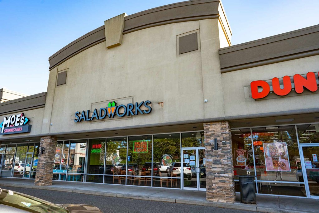 A storefront with a green sign that says "Moes" and a red sign that says "Saladworks" and a brown sign that says "Dunkin Donuts.".