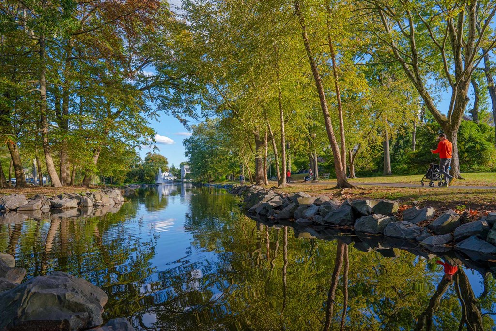 A man in a red shirt is standing by a river with trees on the side.