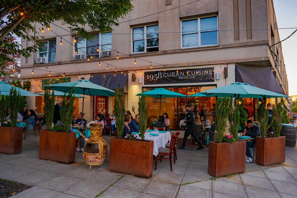 A restaurant with tables and chairs set up outside with green umbrellas.