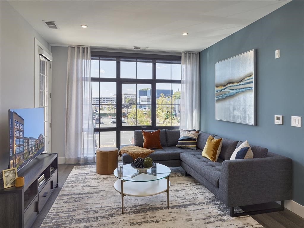 A living room with a grey couch, a glass coffee table, and a large window with a view of the city.