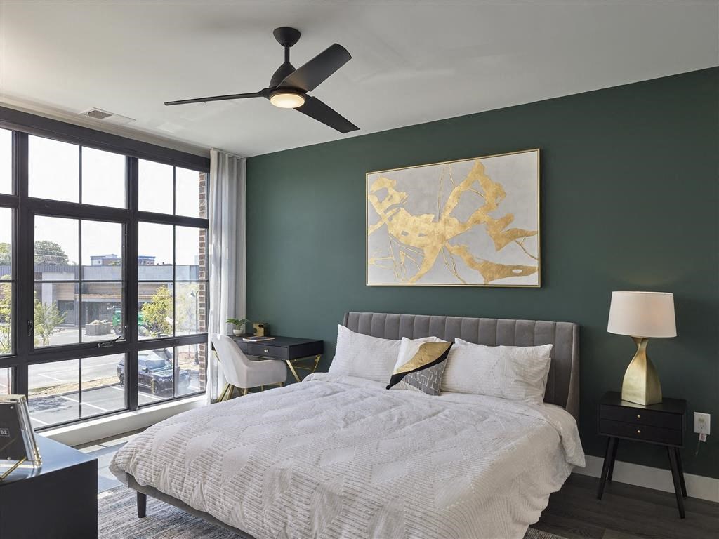 A bedroom with a large bed, a ceiling fan, and a painting on the wall.