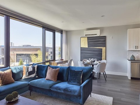 A blue velvet couch with pillows sits in a modern living room with a dining area in the background.