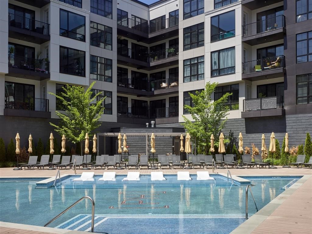 A swimming pool in front of a building with lounge chairs and umbrellas.