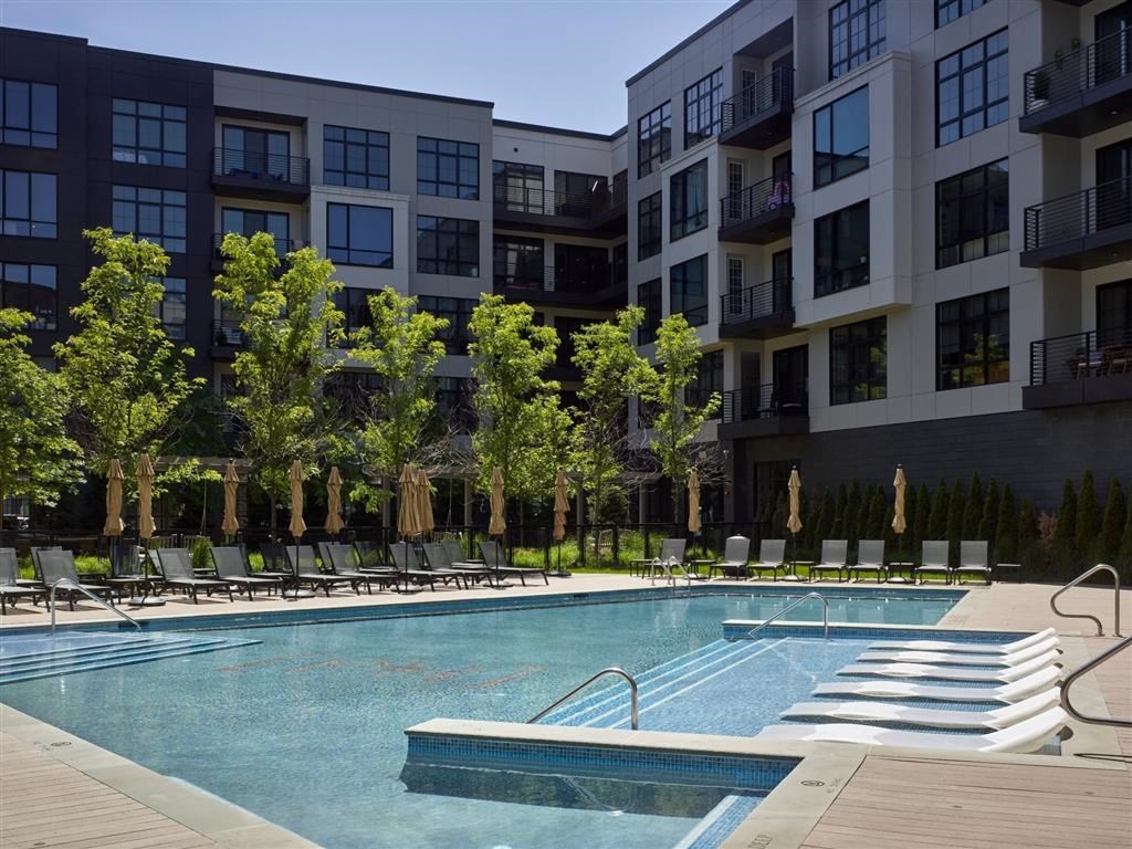 A swimming pool surrounded by lounge chairs and trees in front of apartment buildings.