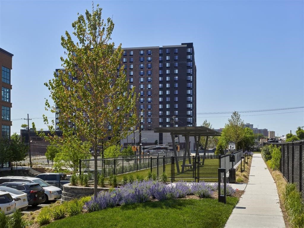 A tall building with a lot of windows is surrounded by a grassy area with trees and a fence.