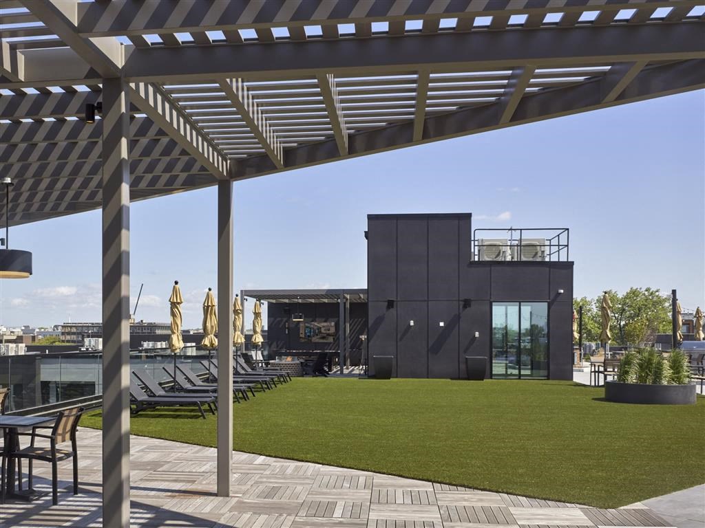 A modern building with a black exterior and a glass facade is surrounded by a well-manicured lawn and outdoor seating area.