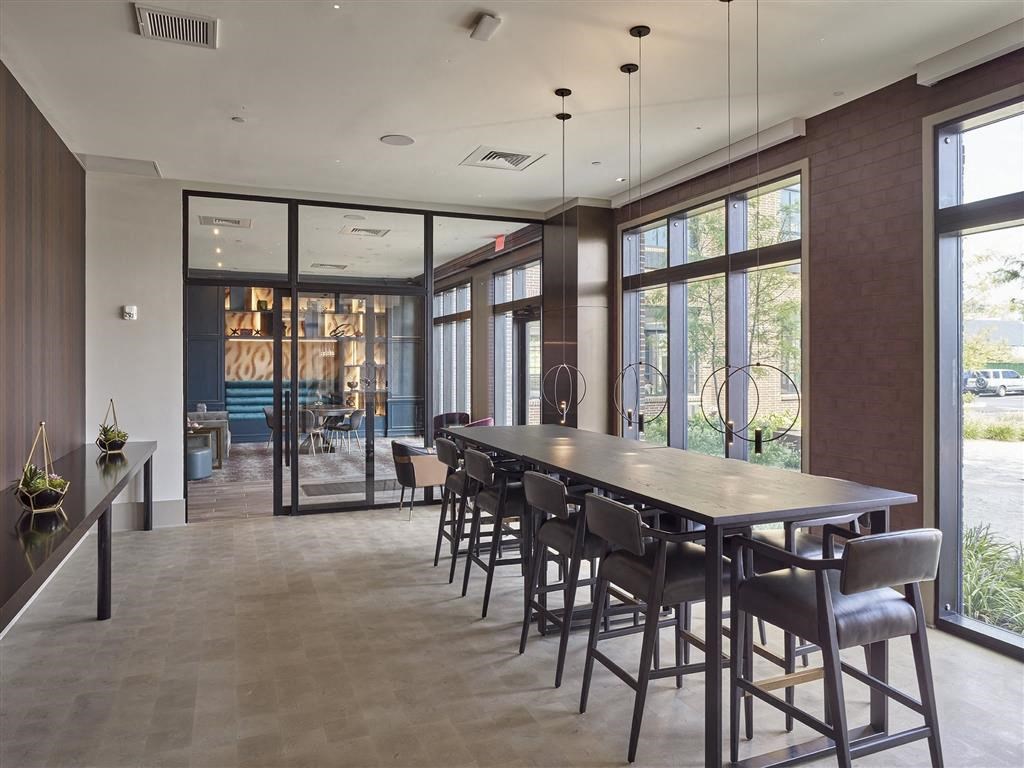 A long wooden table is surrounded by chairs in a room with large windows.