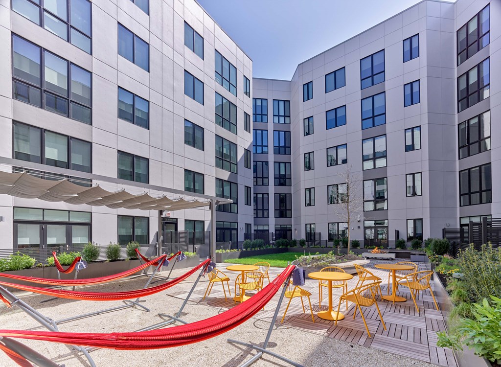 A modern building with a courtyard featuring red hammocks and yellow chairs.