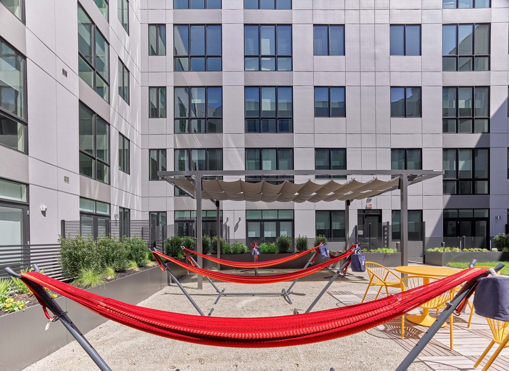 A red hammock is strung between two poles in front of a building.