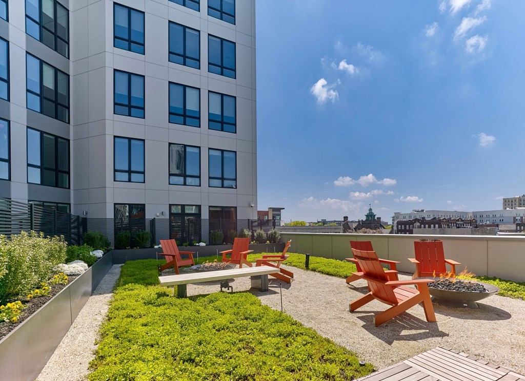 A patio with red chairs and a fire pit in front of a tall building.
