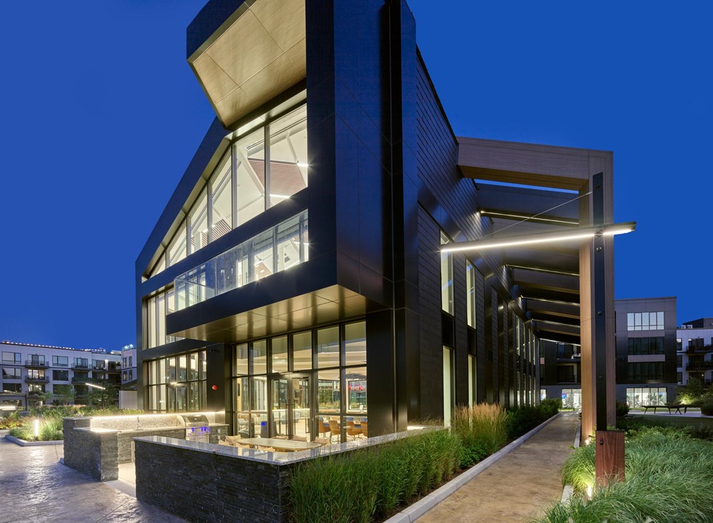 A modern building with a glass facade and a stone base is illuminated from within at night.